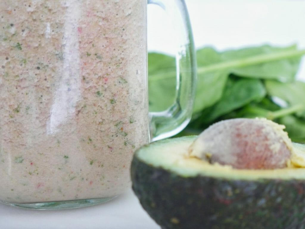 Up-close avocado with smoothie and spinach behind