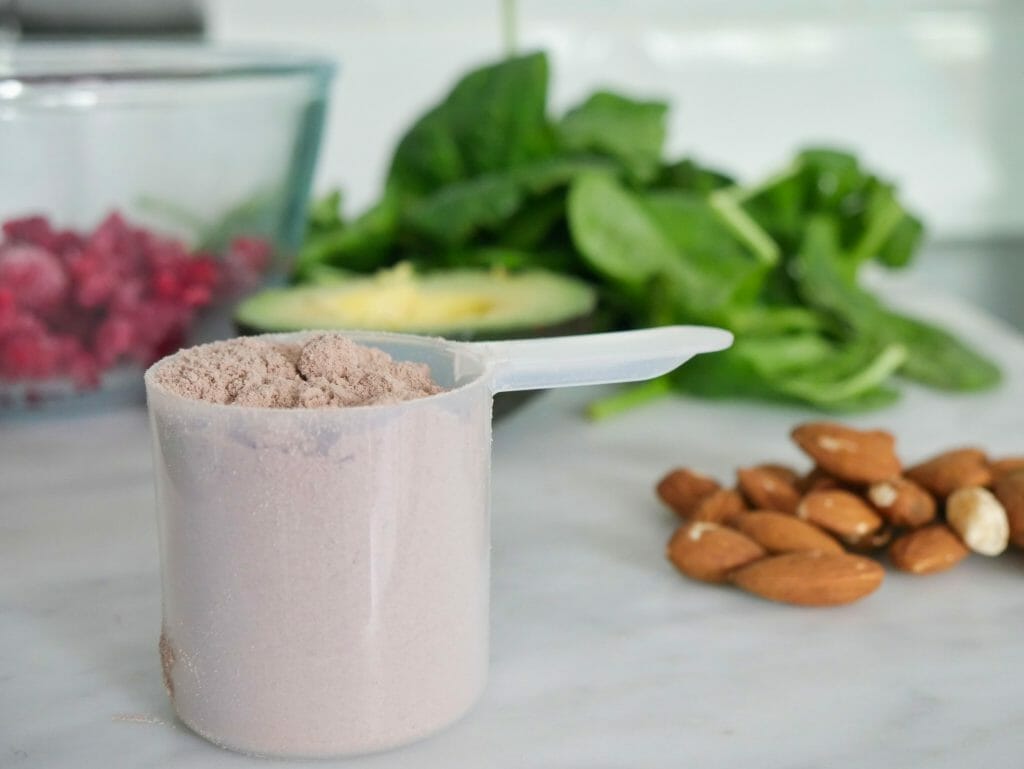 Protein powder with almonds spinach raspberries and avocado behind