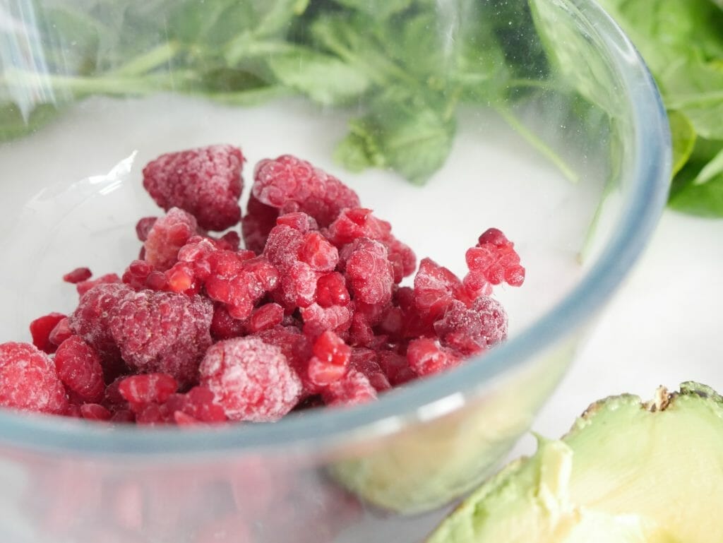 Raspberries in a bowl with avocado and spinach surrounding them