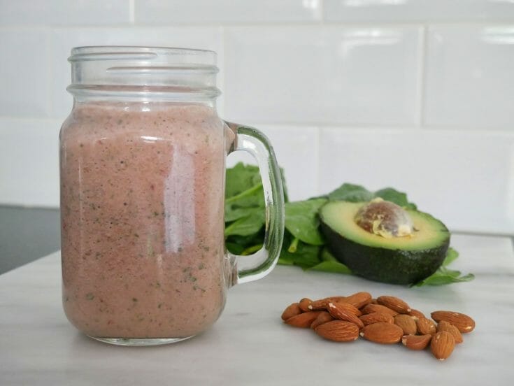An avocado spinach smoothie with raspberries with ingredients around it