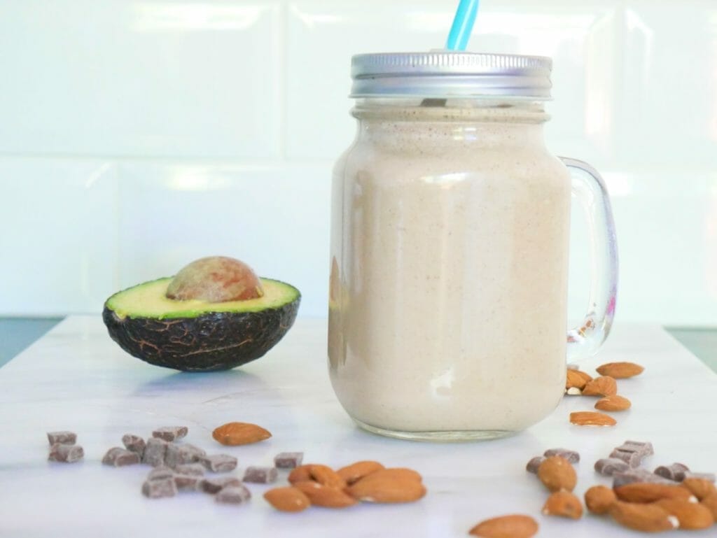 A chocolate almond smoothie with avocado and ingredients around