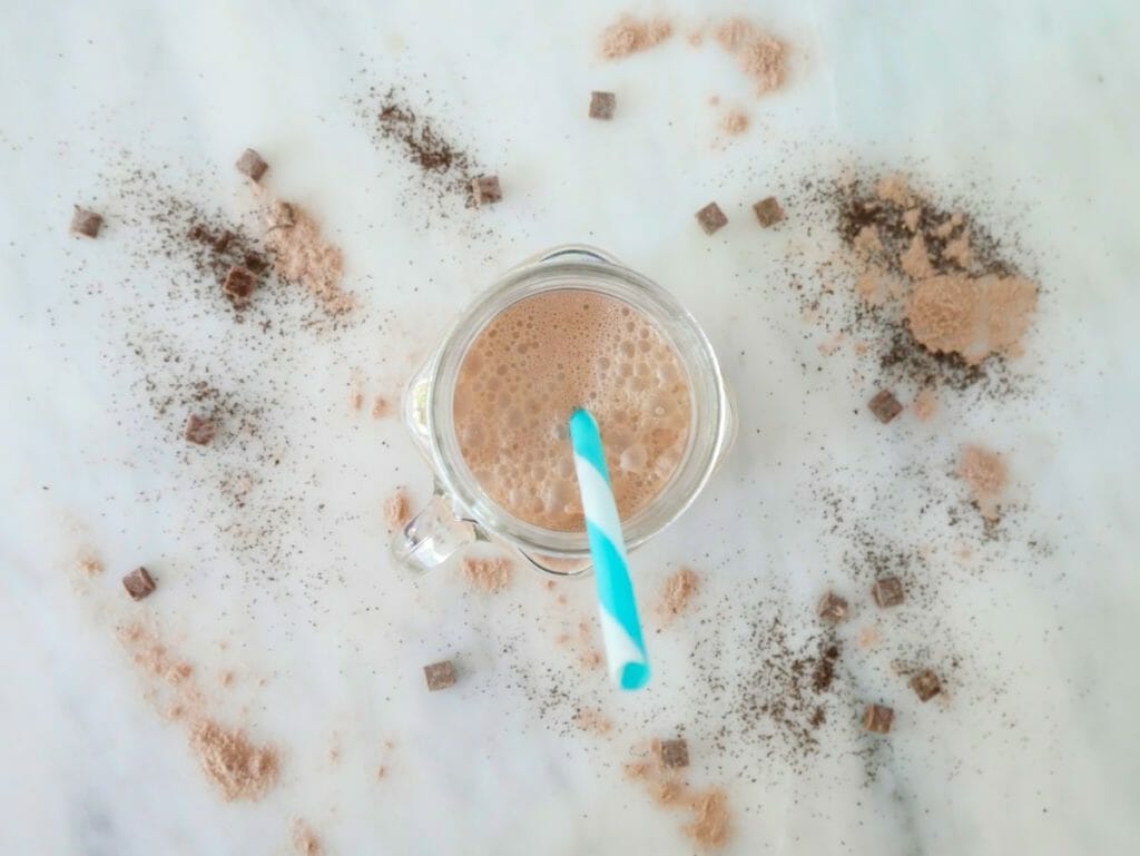 A coffee protein shake with chocolate from above with ingredients scattered around it and a blue straw