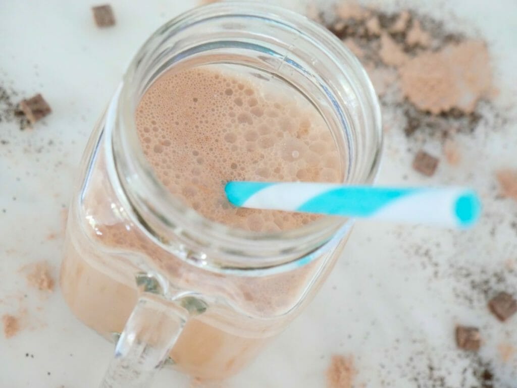 A Keto protein coffee shake on a marble surface with a blue straw and ingredients scattered around it