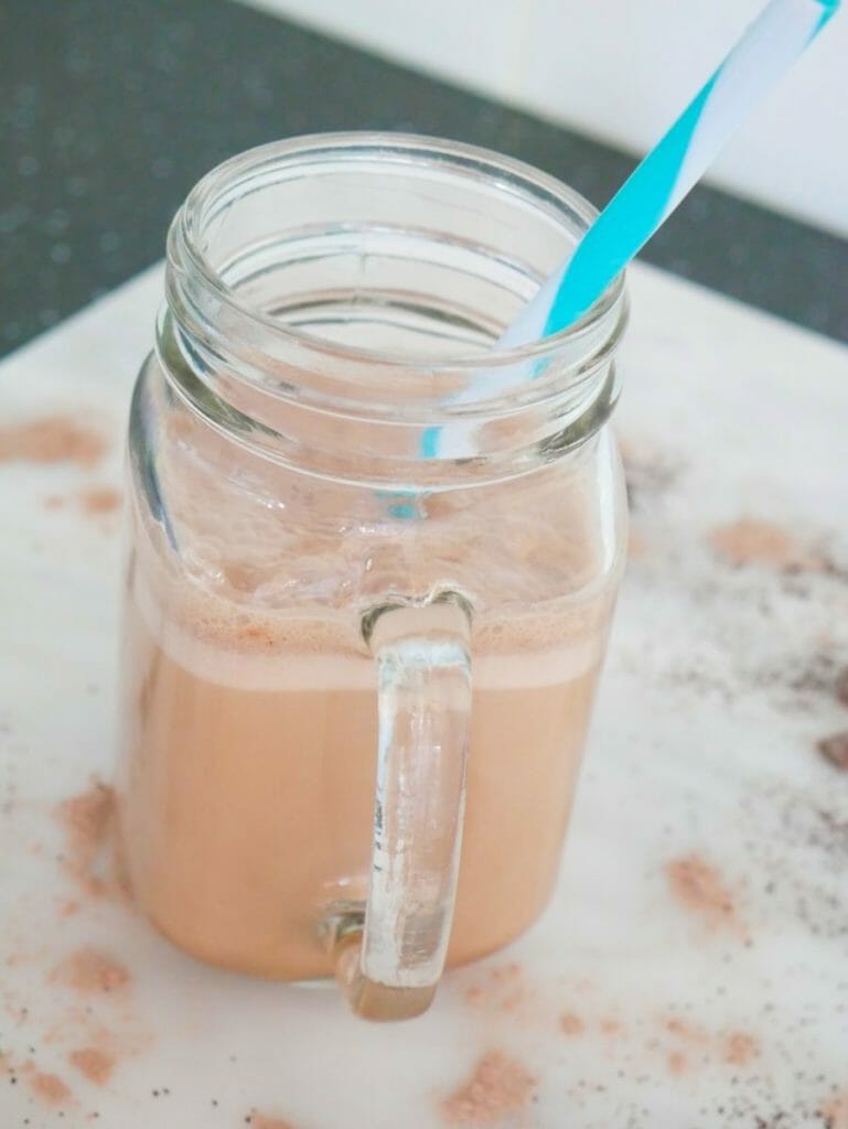 Chocolate coffee protein shake with a blue straw and chocolate around it on a marble surface