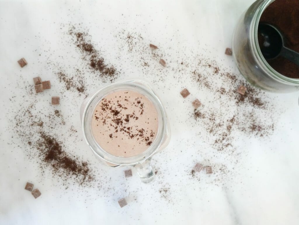 Keto mocha fat bomb smoothie seen from above with chocolate and coffee dusted over and around it on marble