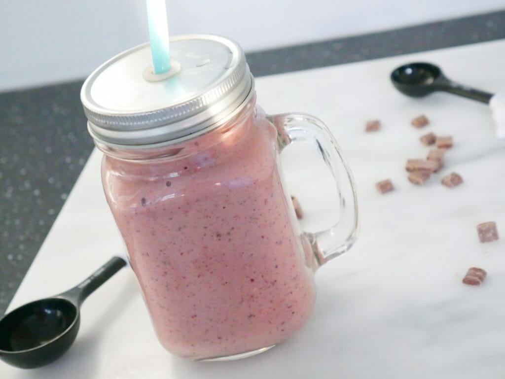 Mixed berry protein smoothie with chocolate with a lid and straw on marble
