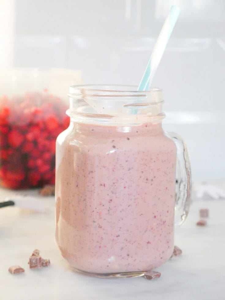Mixed berry protein smoothie with chocolate and raspberries behind