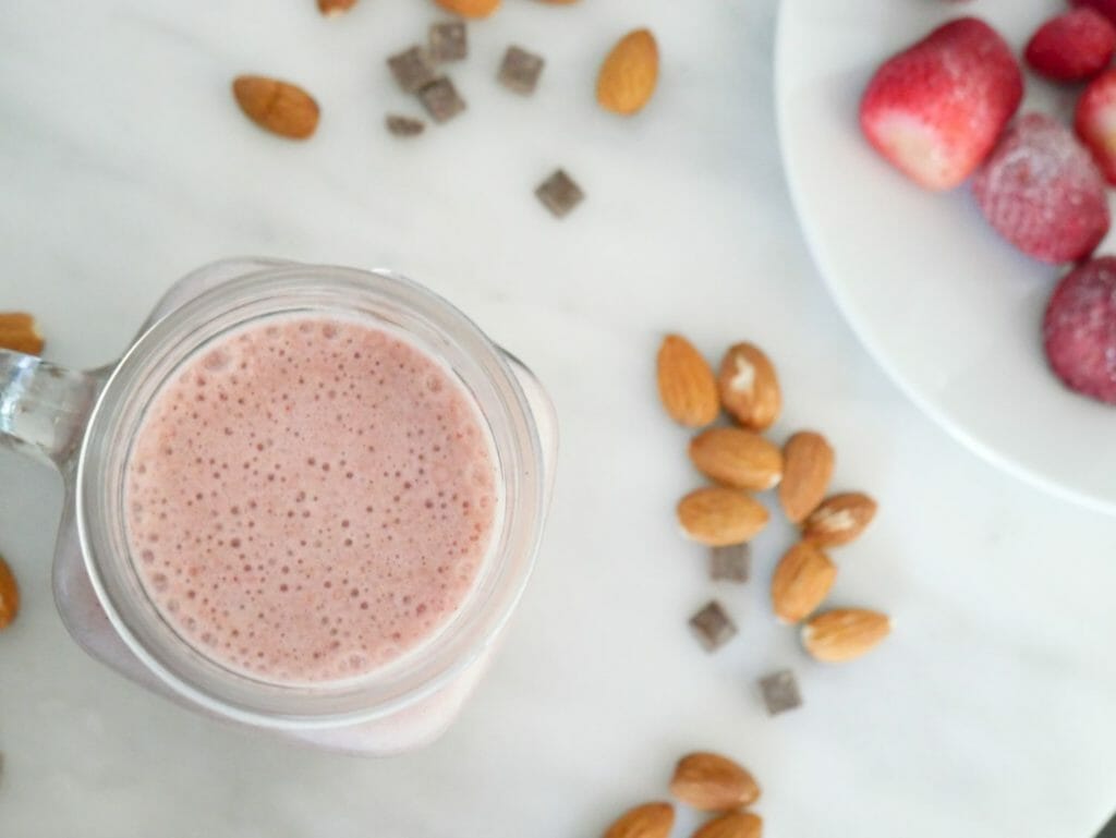 Chocolate strawberry protein smoothie seen from above with almonds and strawberries on marble