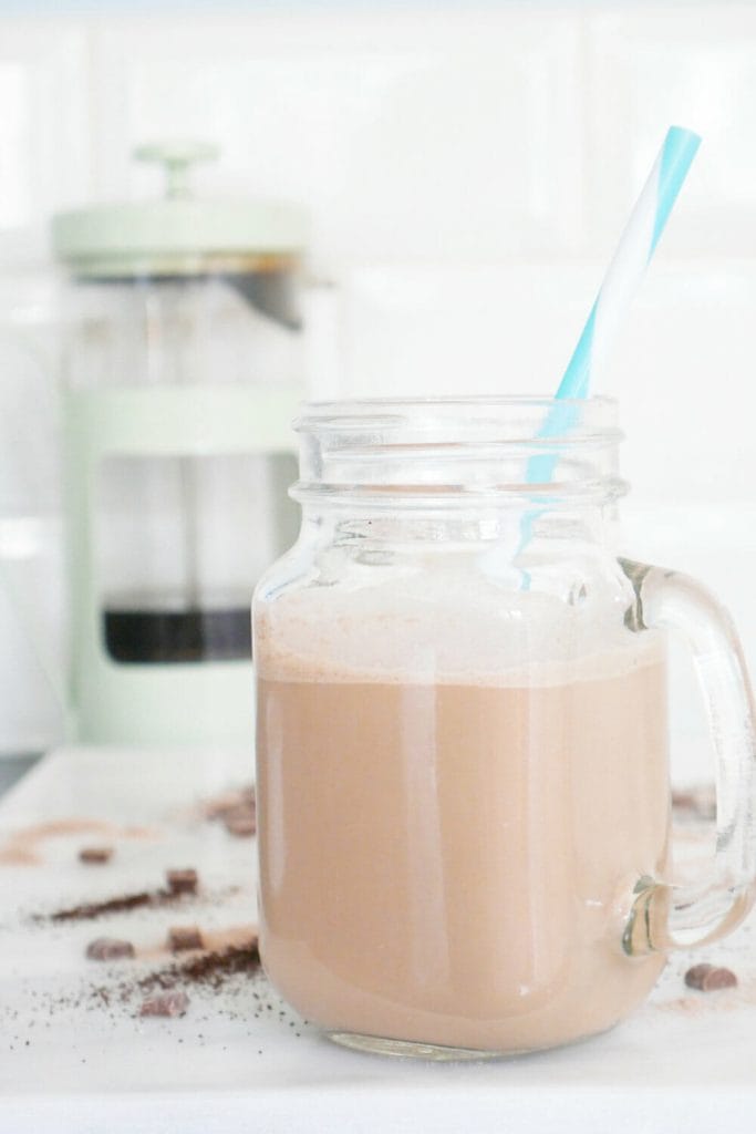 Coffee protein shake smoothie with blue straw and green cafetiere behind