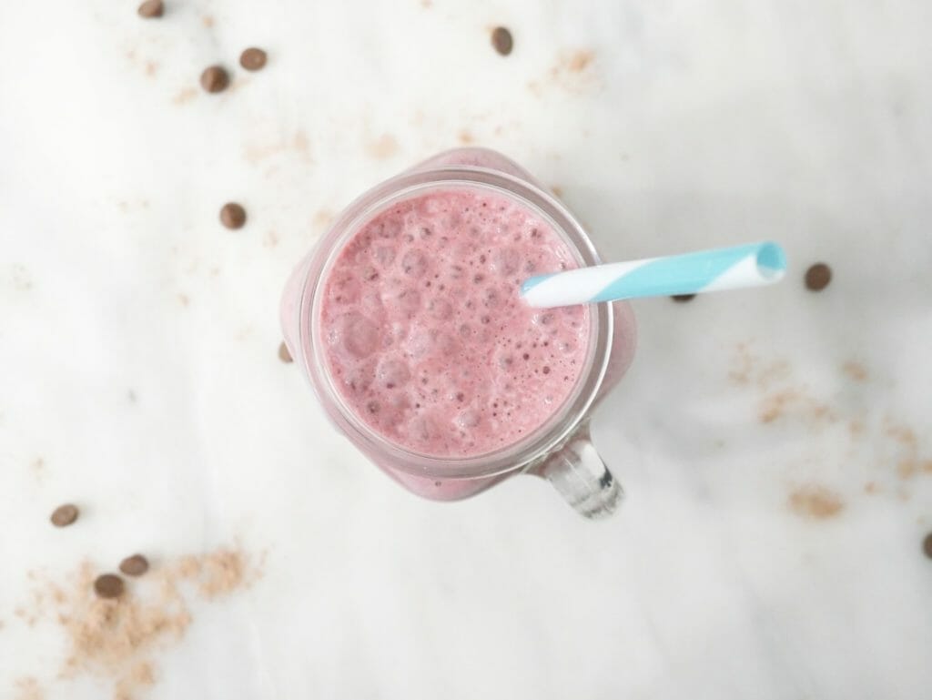 Pink chocolate protein berry weight gain smoothie seen from above with a blue straw