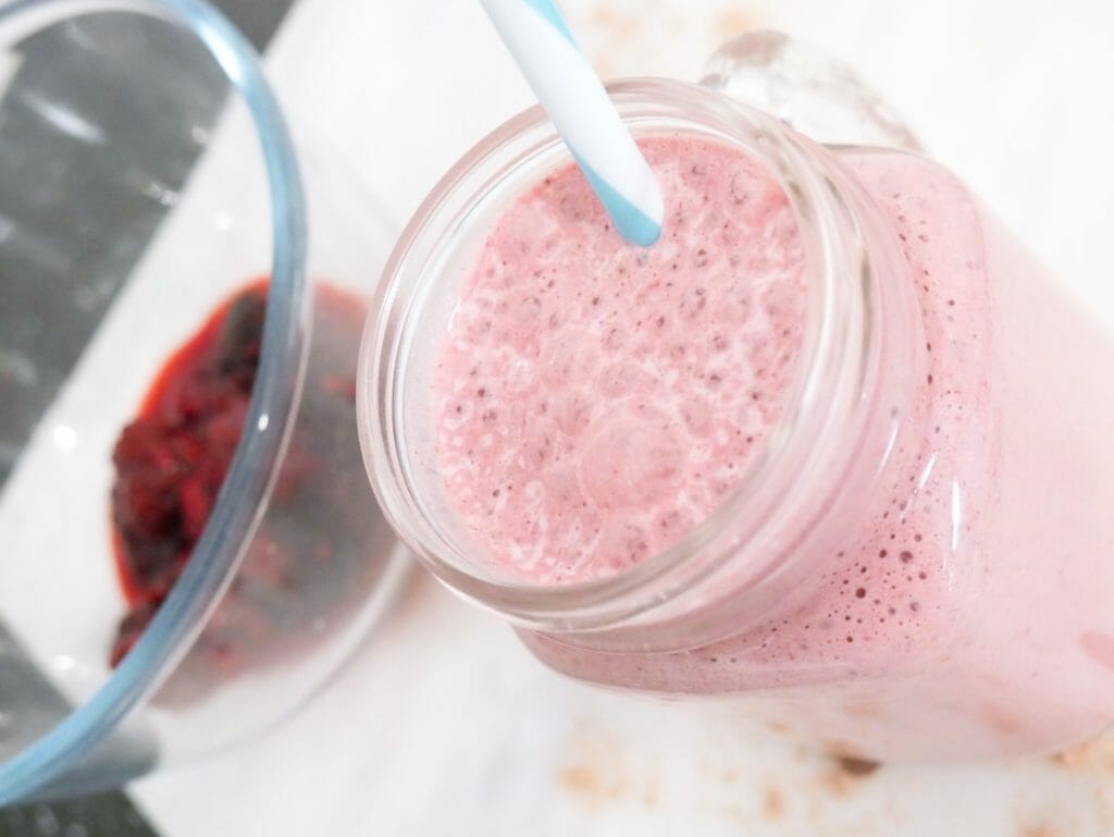 Frozen berry protein smoothie for weight gain from above with a blue straw and berries behind