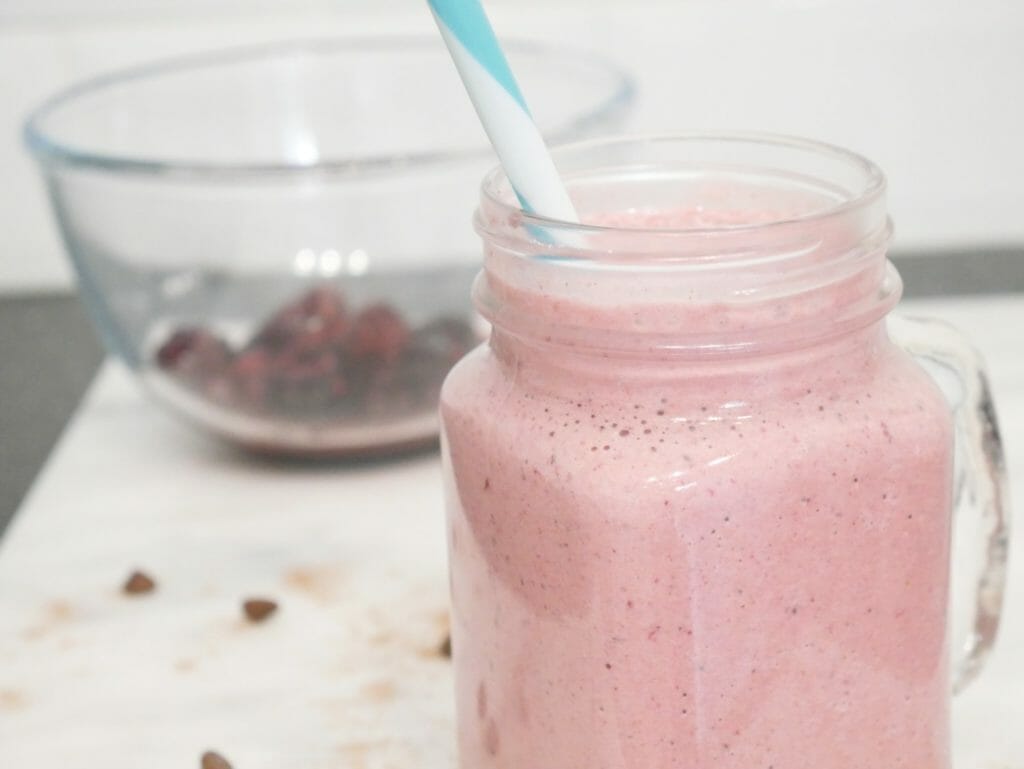Pink high fat protein shake with berries behind