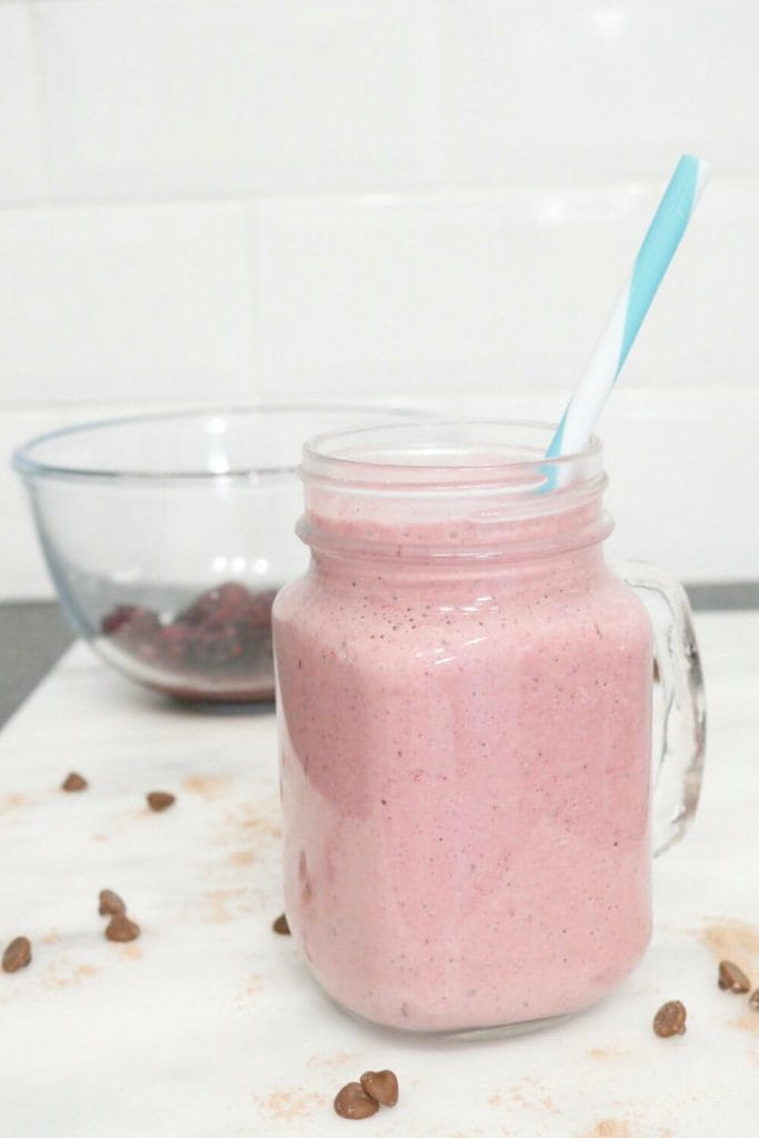Chocolate protein berry weight gain smoothie with berries in a bowl behind