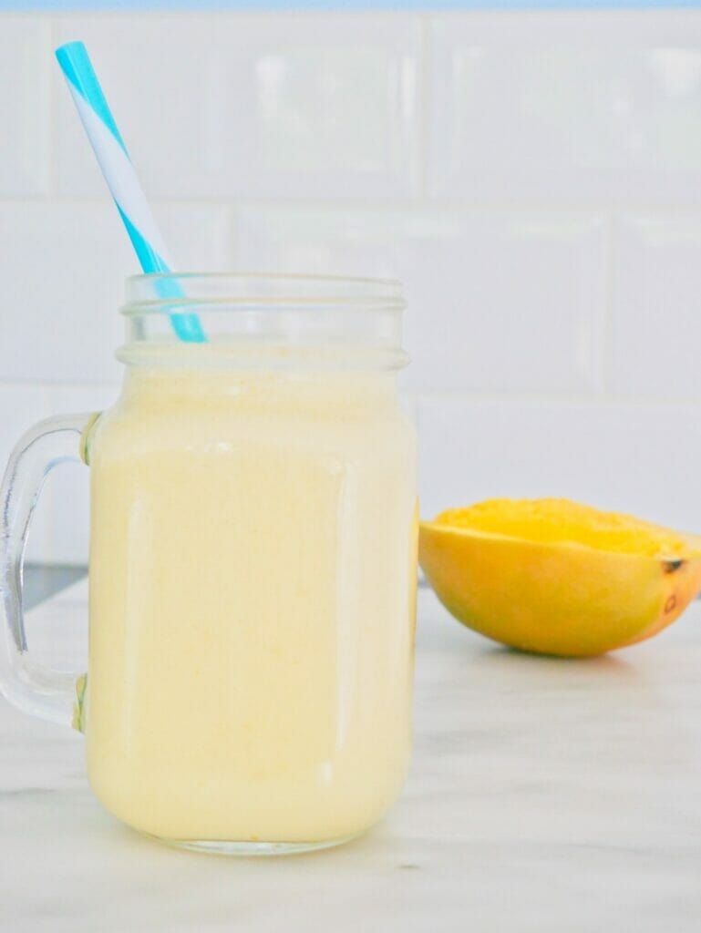 A coconut mango smoothie with mango behind and blue straw