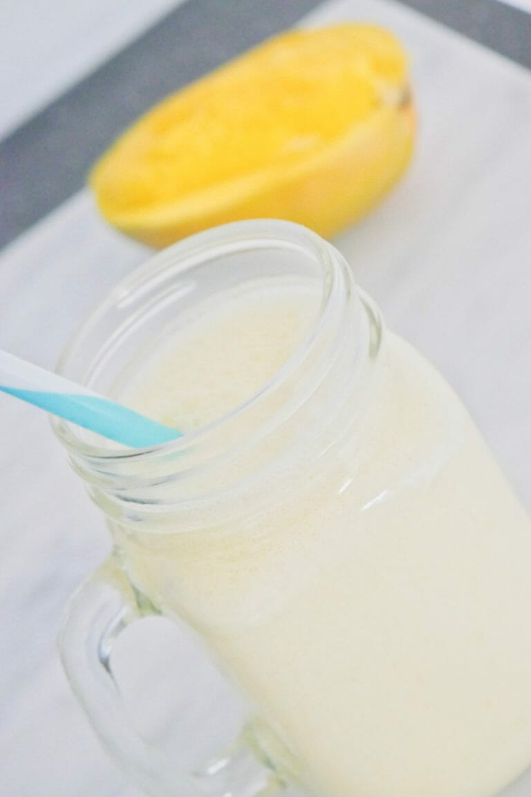 Coconut mango smoothie recipe with mango behind and a blue straw