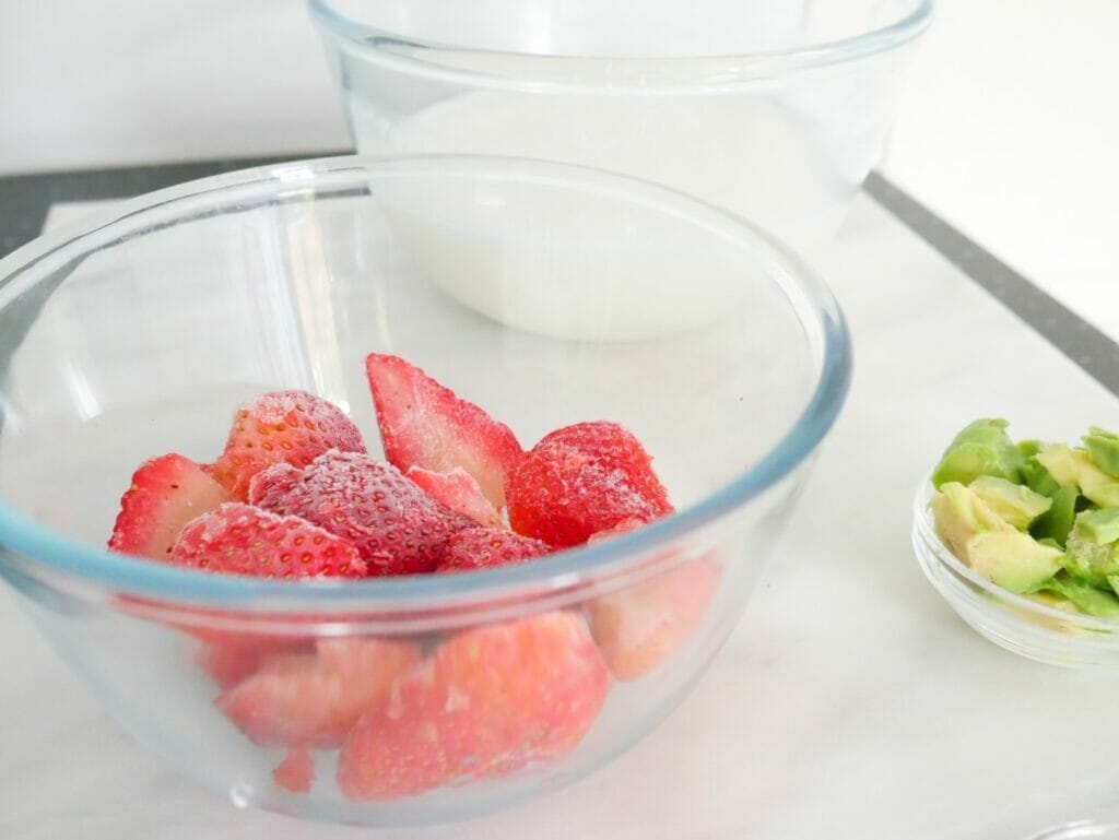 Frozen strawberries in a bowl, with coconut milk and avocado for a Keto strawberry coconut milk smoothie