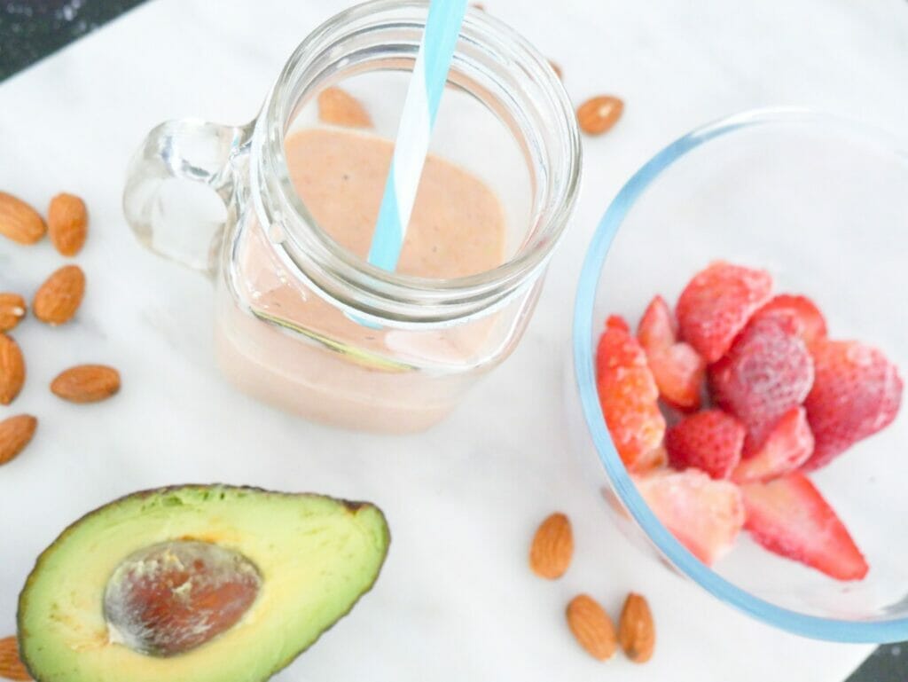 A keto strawberry smoothie with coconut milk and avocado and almonds on marble