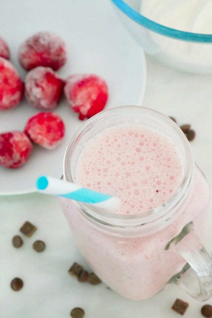 Strawberry coconut smoothie with chocolate with ingredients around from above with a blue and white sraw