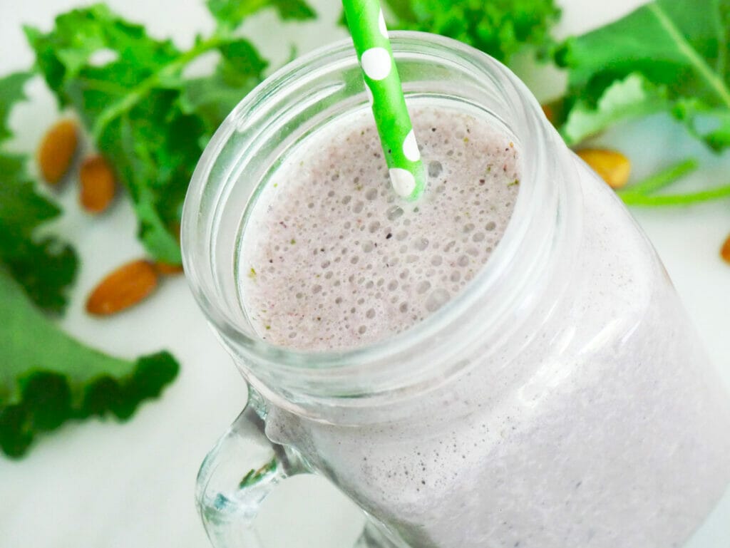 Kale and berry smoothie with ingredients behind