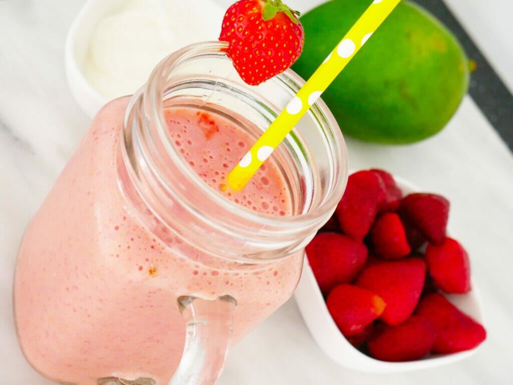 Healthy mango strawberry smoothie with ingredients behind