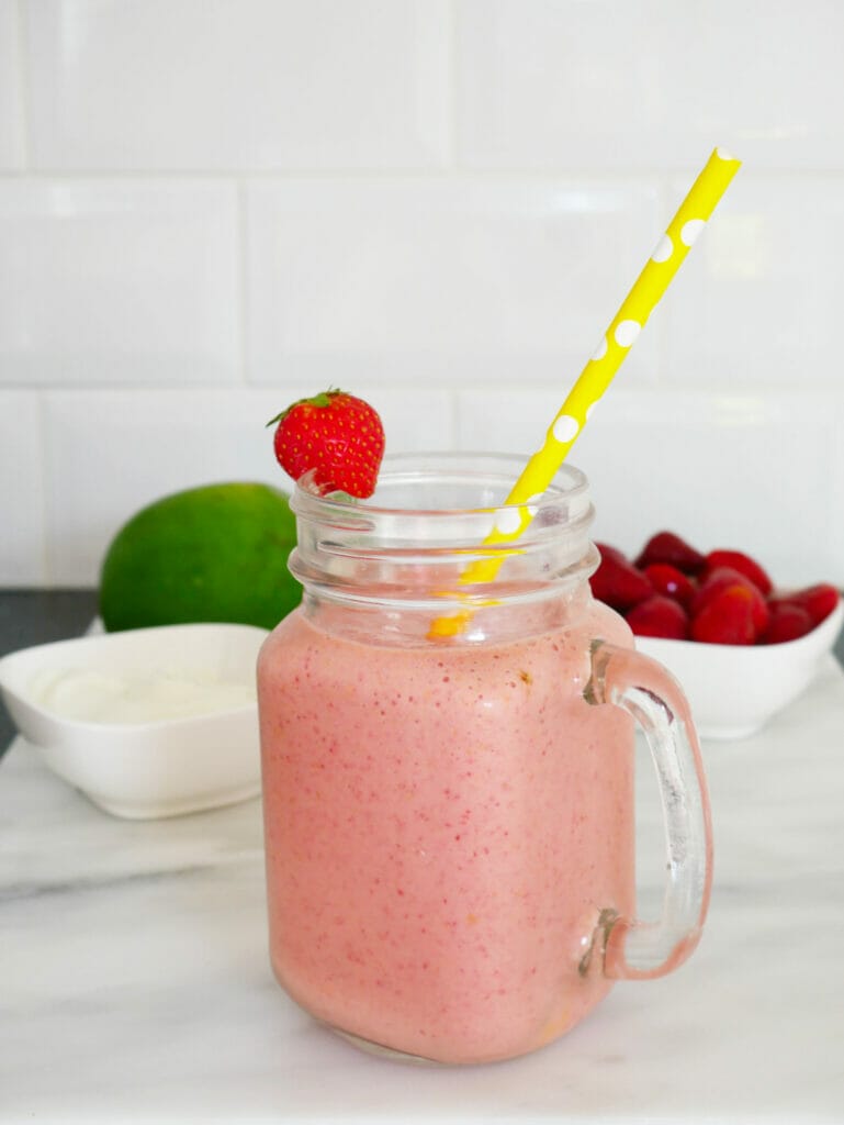 Strawberry mango smoothie with yellow straw and strawberries and mango behind
