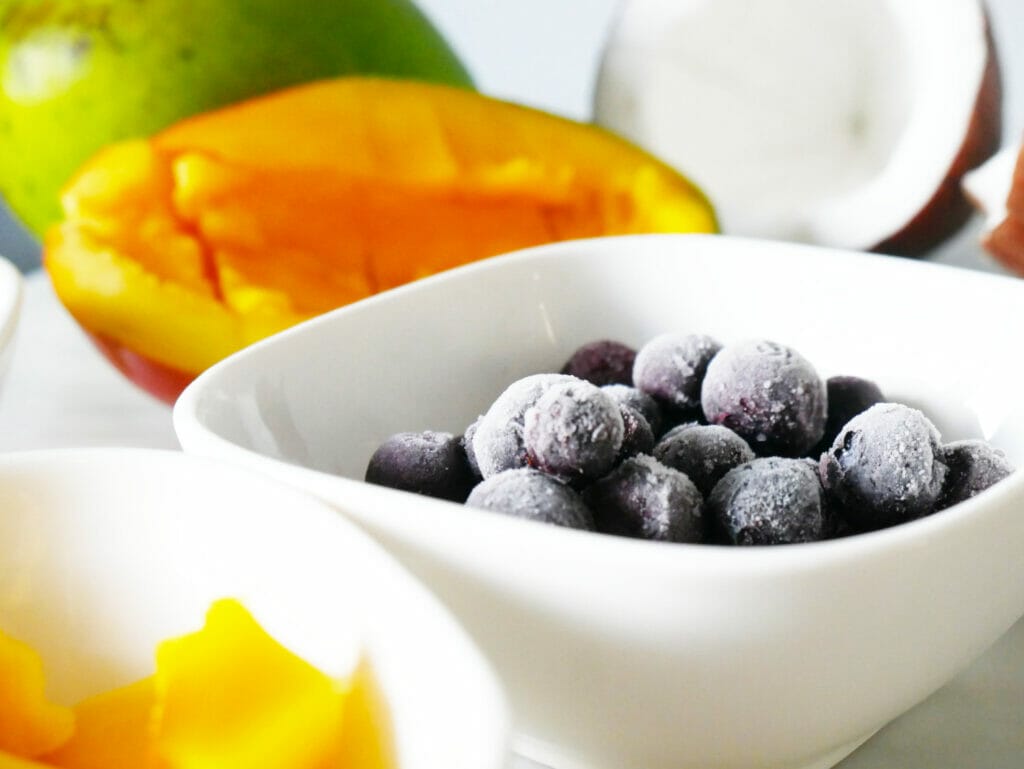 Blueberries in a dish with mango and coconut behind