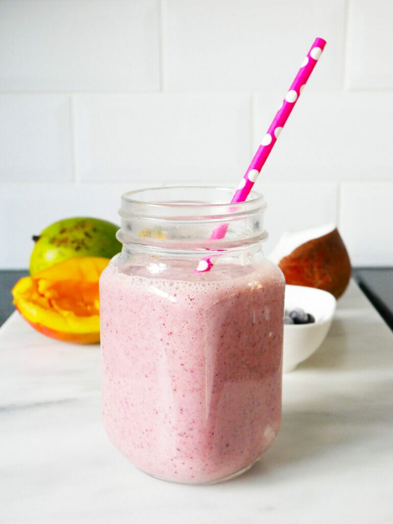 Mango blueberry smoothie in front of ingredients with red pink straw