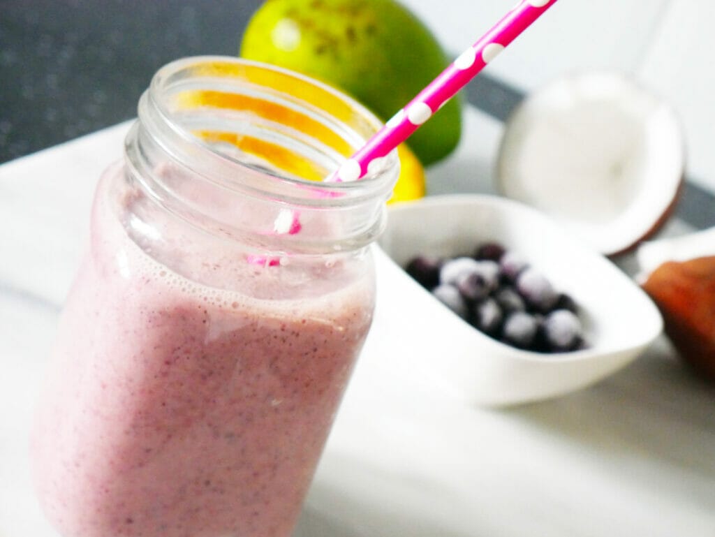 Blueberry mango smoothie in front of ingredients with red straw