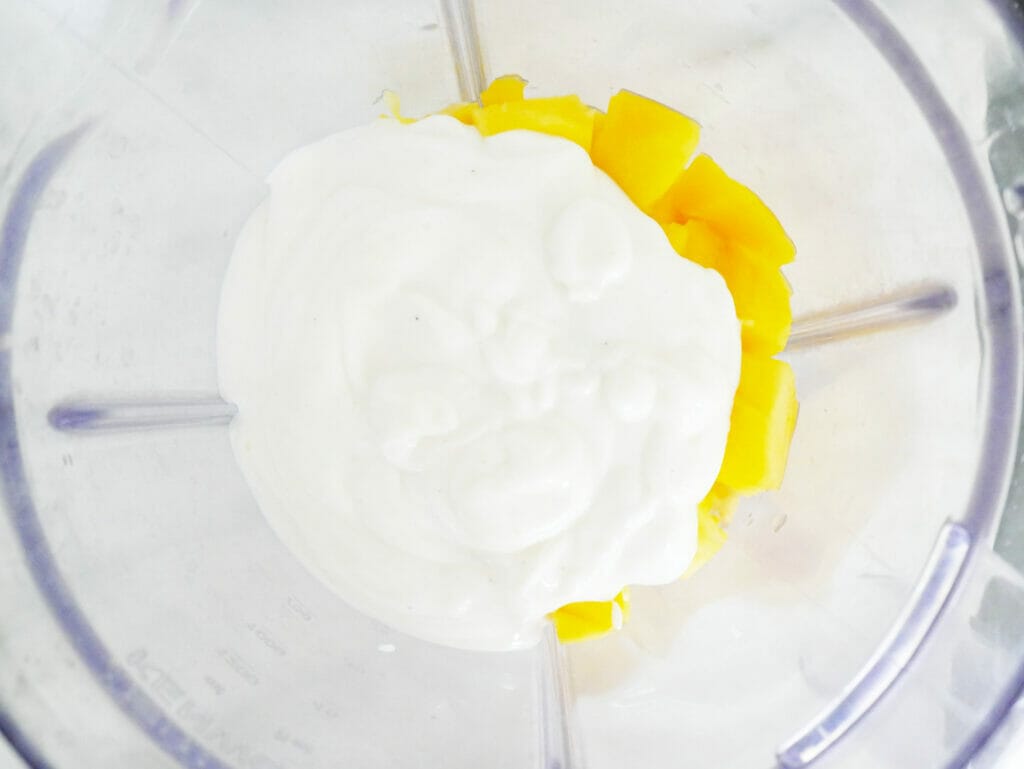 Coconut yogurt mango and pineapple in a blender for a smoothie