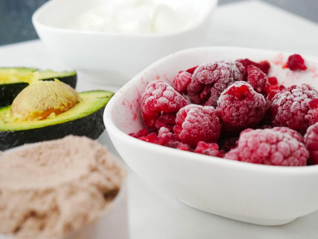 Raspberries in a container with avocado and chocolate protein powder