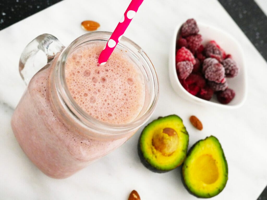 Red straw coming out of weight gain shake with raspberries almonds and avocado