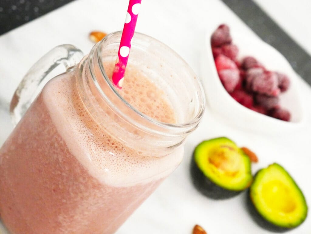 Chocolate raspberry smoothie weight gainer shake with avocado and raspberries behind