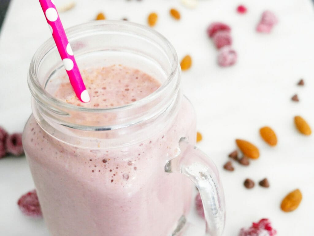 Keto chocolate protein shake with almonds and raspberries and red straw